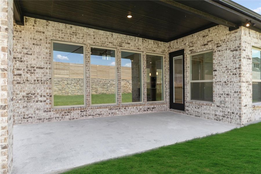Covered back patio with concrete slab, brick exterior, large windows, and back door entry to home