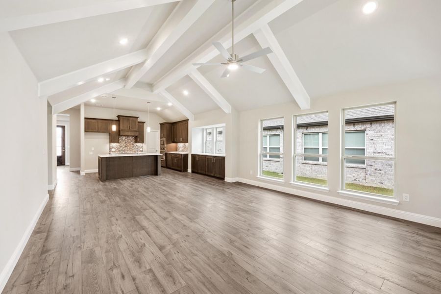 Open living area with vaulted beamed ceiling, hardwood floors, and open kitchen with dark cabinets and island