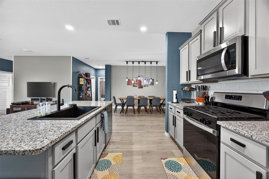 Kitchen with stainless steel appliances, light stone countertops, light wood-style floors, a center island with sink, and gray cabinets