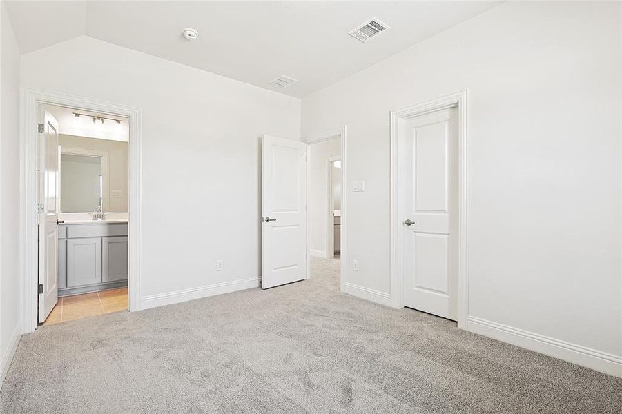 Unfurnished bedroom featuring lofted ceiling, light carpet, and ensuite bathroom