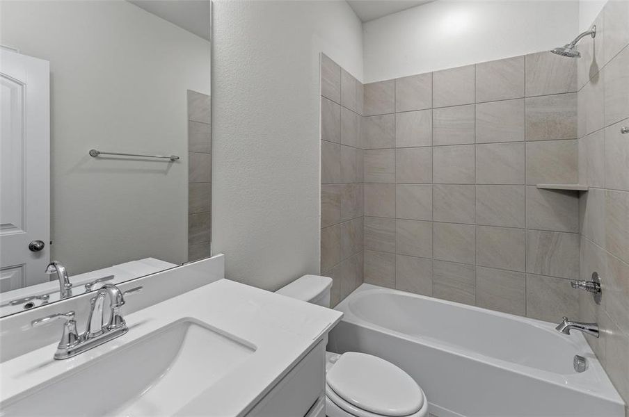 Full bathroom featuring a single vanity with an integrated sink and chrome fixtures, a toilet, and a combination tub and shower with tile surround and a recessed shelf Full bathroom featuring a single vanity with an integrated sink and chrome fixtures, a toilet, and a combination tub and shower with tile surround and a recessed shelf