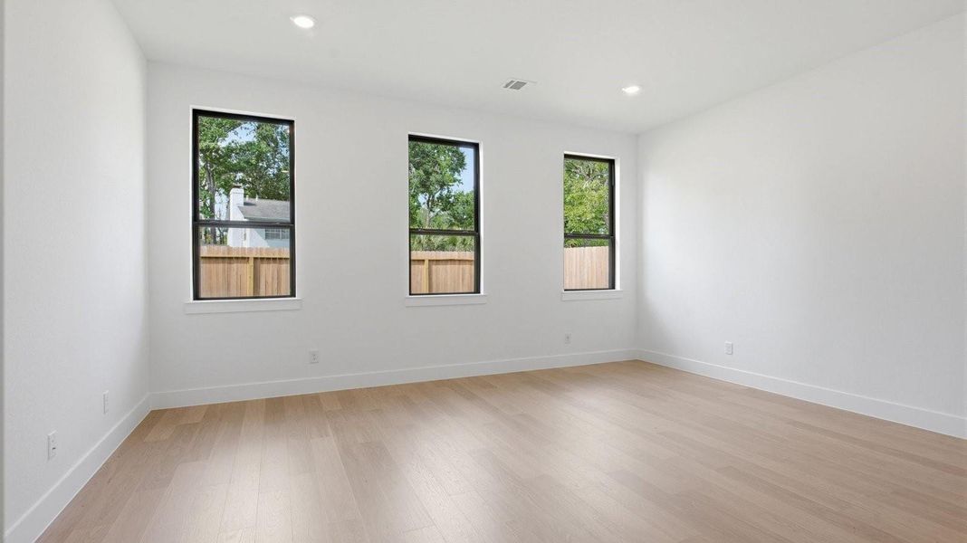 The primary bedroom with ceiling fan, three large windows for natural lighting, hardwood floors, and a large walk-in closet.