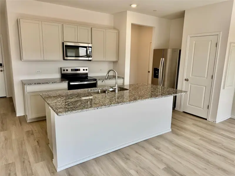 Kitchen featuring stainless steel appliances, light stone countertops, light wood-type flooring, an island with sink, and recessed lighting Kitchen featuring stainless steel appliances, light stone countertops, light wood-type flooring, an island with sink, and recessed lighting