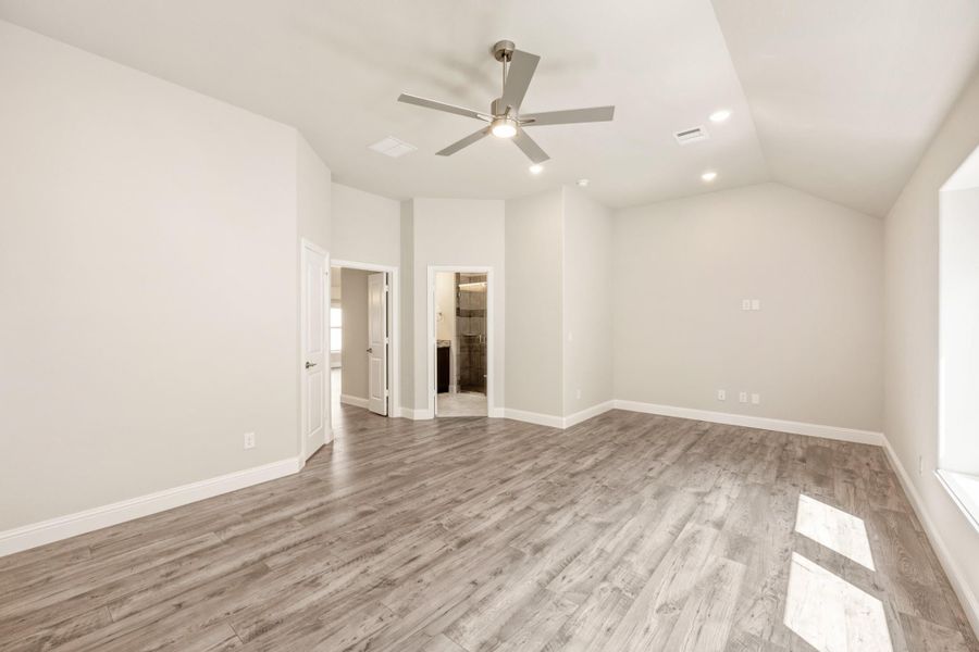 Empty master bedroom with vaulted ceiling, ceiling fan, wood-look floors, and open ensuite bathroom door