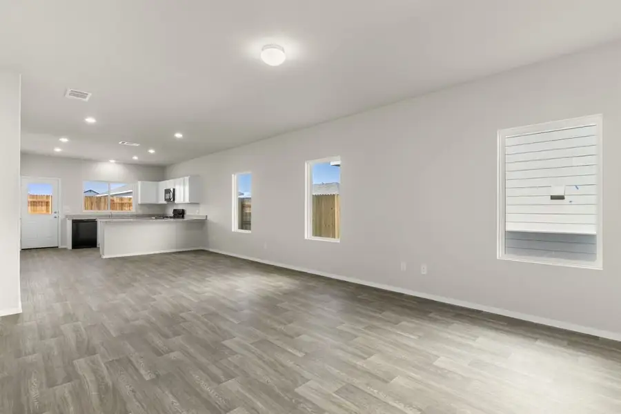 Image of a living room with beige walls, brown wood-look flooring, three windows, and a connecting open kitchen Image of a living room with beige walls, brown wood-look flooring, three windows, and a connecting open kitchen