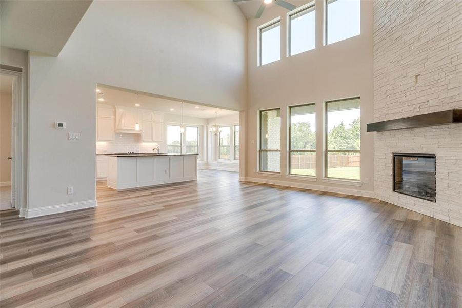 Unfurnished living room featuring a fireplace, light wood-type flooring, sink, a high ceiling, and ceiling fan