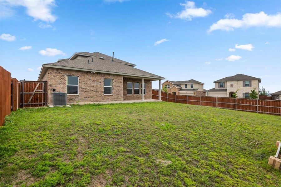Expansive backyard featuring a grass lawn, wood privacy fencing, and a covered patio