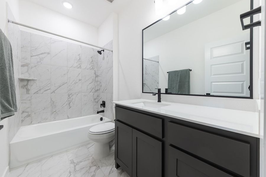 Guest bathroom with shower/bathtub combination, light marble finish floors, and vanity
