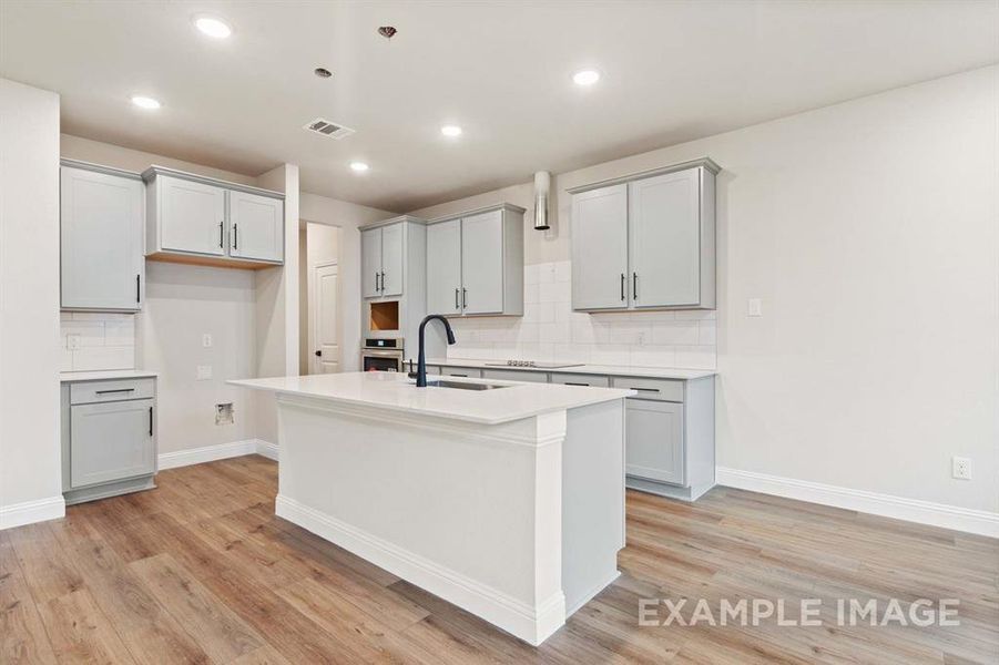 Kitchen with decorative backsplash, a center island with sink, gray cabinetry, and sink