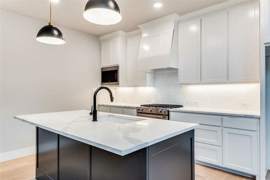 Kitchen with light hardwood / wood-style flooring, backsplash, a kitchen island with sink, appliances with stainless steel finishes, and pendant lighting