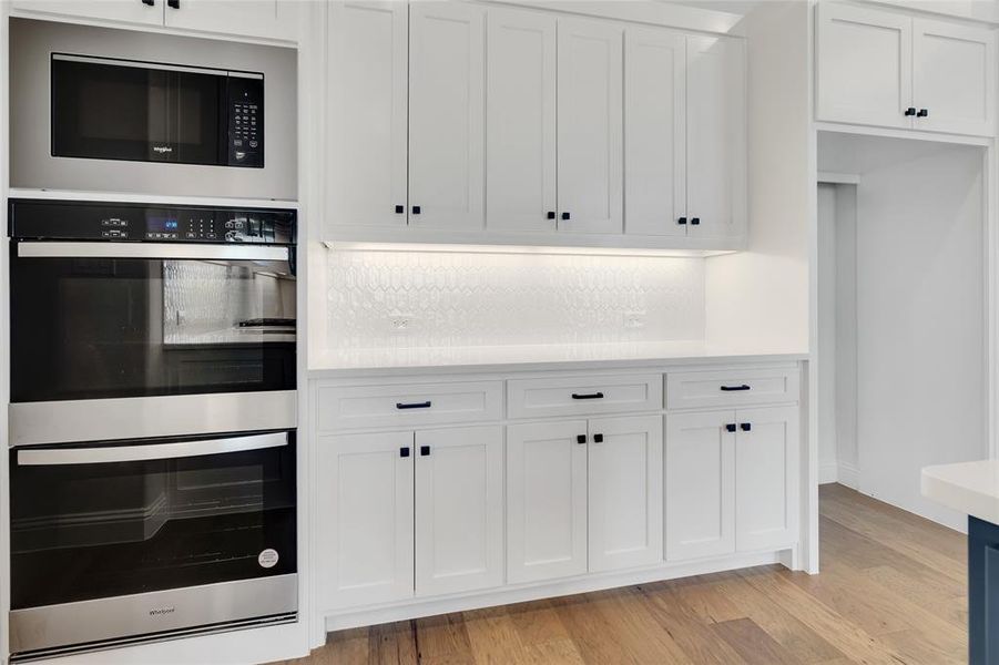 Kitchen featuring light hardwood / wood-style floors, black microwave, stainless steel double oven, backsplash, and white cabinets