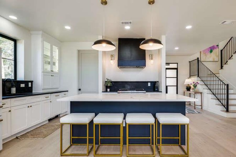 Kitchen featuring a kitchen breakfast bar, white cabinetry, light wood-style flooring, pendant lighting, and ventilation hood
