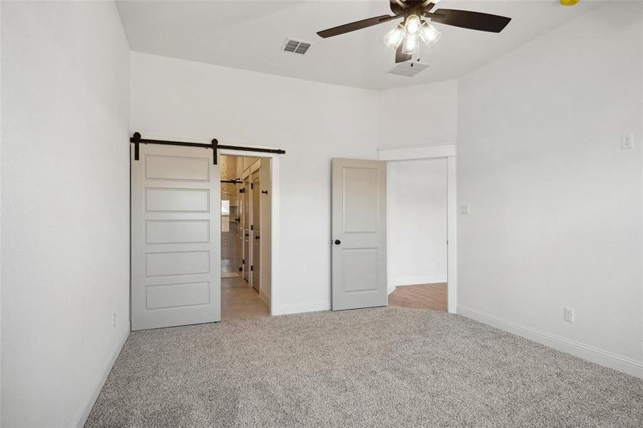 Unfurnished bedroom featuring a barn door, ceiling fan, and light colored carpet