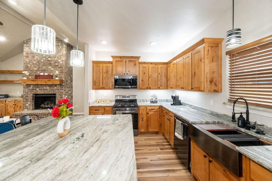 Kitchen with light stone counters, stainless steel appliances, decorative light fixtures, and light hardwood / wood-style flooring