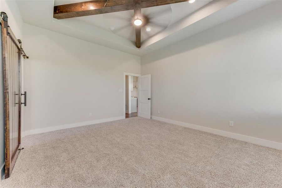 Unfurnished room with carpet flooring, ceiling fan, a barn door, a tray ceiling, and beamed ceiling