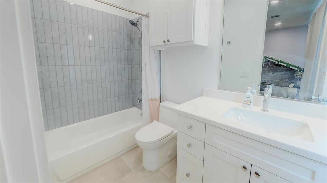 This bathroom features a modern design with a sleek white vanity, integrated sink, and ample cabinet space. It includes a shower-tub combo with contemporary tilework and a large mirror, creating a bright and clean atmosphere.