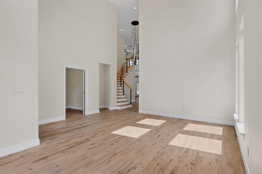 Spare room featuring a towering ceiling, light wood-type flooring, and stairway Spare room featuring a towering ceiling, light wood-type flooring, and stairway