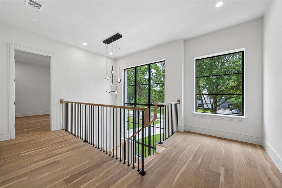 A striking two story staircase is framed by a custom specialty window unit - lifted into place by crane - that fills the landing with natural light. LED lighting and custom fabricated stair nosing milled from the flooring itself pair with a white oak handrail and metal balusters and posts for a clean architectural statement. An open upper landing enhances the home’s airy, connected design.