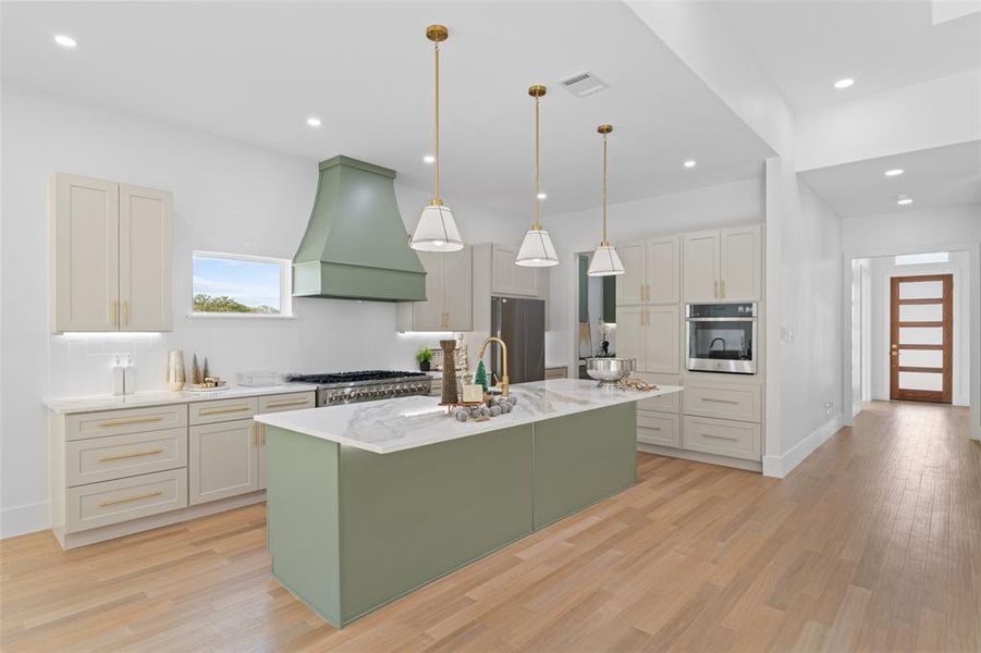 Kitchen featuring green cabinetry, decorative light fixtures, a center island with sink, light stone countertops, and light wood-type flooring