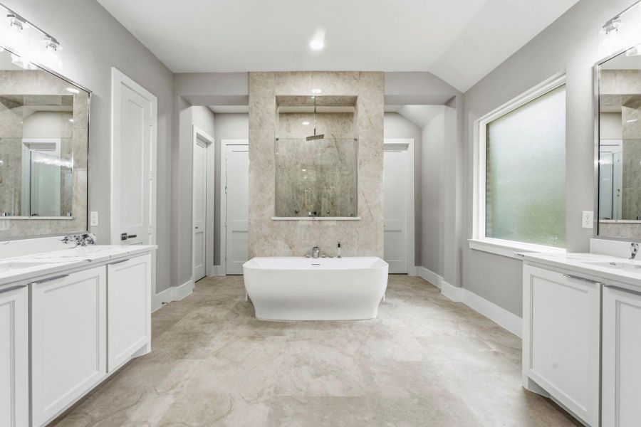A spa inspired primary bath centers around a sculptural freestanding soaking tub, framed by a striking stone shower wall. Separate vanities and generous storage give the space both beauty and function.