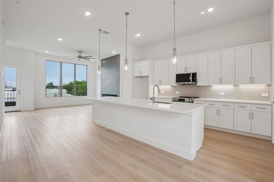 Kitchen with decorative light fixtures, white cabinetry, backsplash, a kitchen island with sink, and recessed lighting