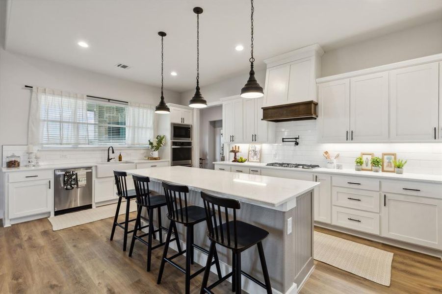 Spacious kitchen featuring an expansive central island with seating, white shaker cabinetry, stainless steel appliances, and wood-finish flooring