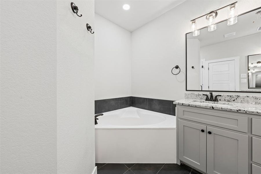 Bathroom with a garden tub, vanity, and dark tile patterned floors Bathroom with a garden tub, vanity, and dark tile patterned floors