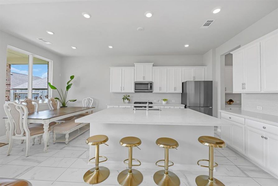 The modern bright kitchen featuring white cabinets, gorgeous countertops,  stainless steel appliances and a large island with bar seating. The adjoining breakfast area flows with natural light and has great views of the backyard.