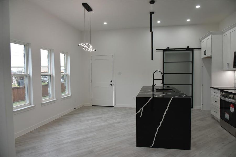 Kitchen with electric stove, a barn door, decorative light fixtures, white cabinets, and an island with sink