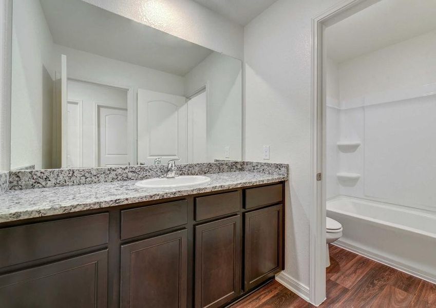 Rio bathroom with large granite vanity top, brown custom cabinets, and fixed wall light