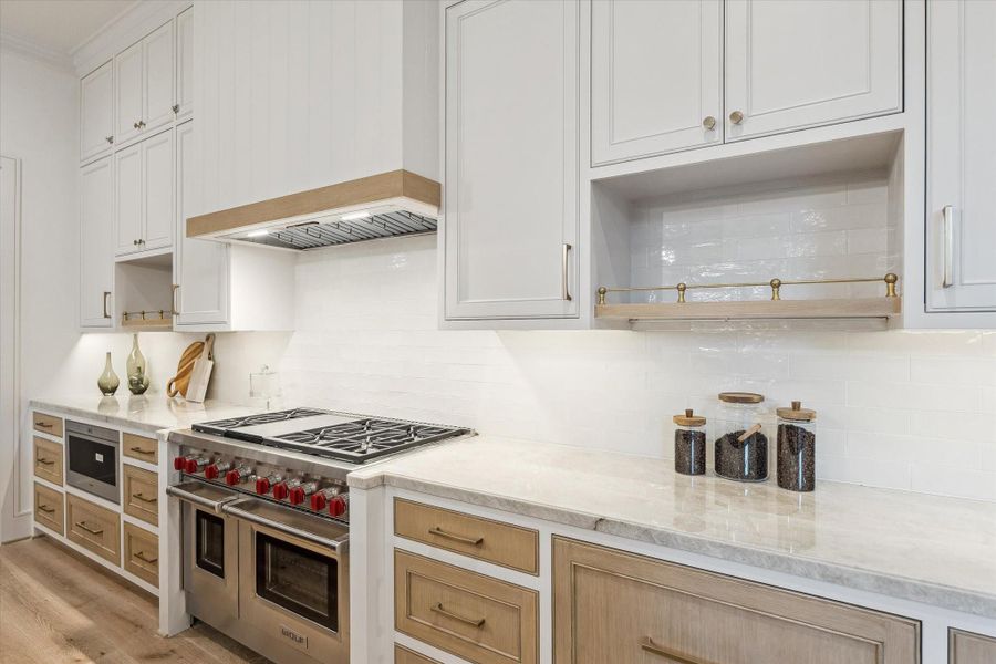 A closer look at the stainless appliances. The professional quality rangehood is encased in white trim for a seamless appearance. The Wolf microwave and 6-burner, two oven gas range also includes an infrared grill. White oak drawers and shelves and brass accents bring a modern touch.