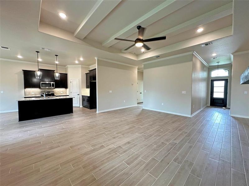 Unfurnished living room with crown molding, ceiling fan, light wood finished floors, a raised ceiling, and recessed lighting