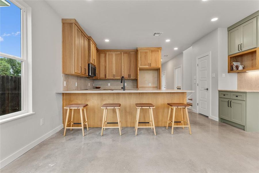 Kitchen featuring tasteful backsplash, a peninsula, a breakfast bar area, concrete floors, and recessed lighting Kitchen featuring tasteful backsplash, a peninsula, a breakfast bar area, concrete floors, and recessed lighting