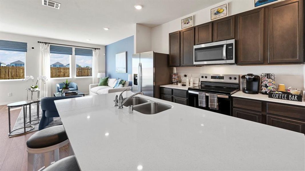 Kitchen with dark wood finish cabinets, stainless steel appliances, light wood-style flooring, recessed lighting, and a kitchen bar
