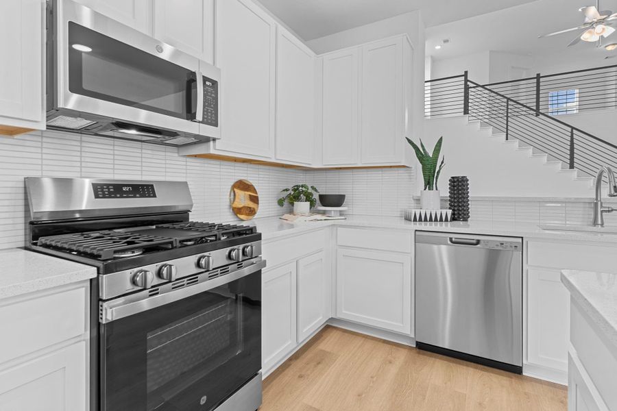 A close-up view showcases the stainless steel appliance package including a freestanding gas range, microwave, and dishwasher—complemented by a ceramic tile backsplash and 42” white cabinets for a fresh, modern look. **Image Representative of Plan Only and May Vary as Built**.