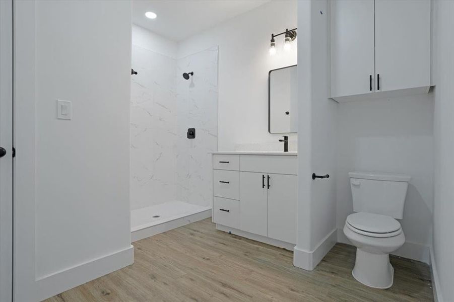 Bathroom featuring vanity, toilet, wood-type flooring, and tiled shower