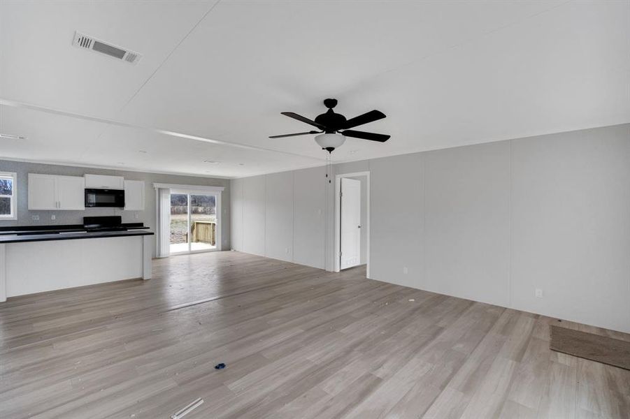 Unfurnished living room with a decorative wall, light wood-style flooring, and ceiling fan