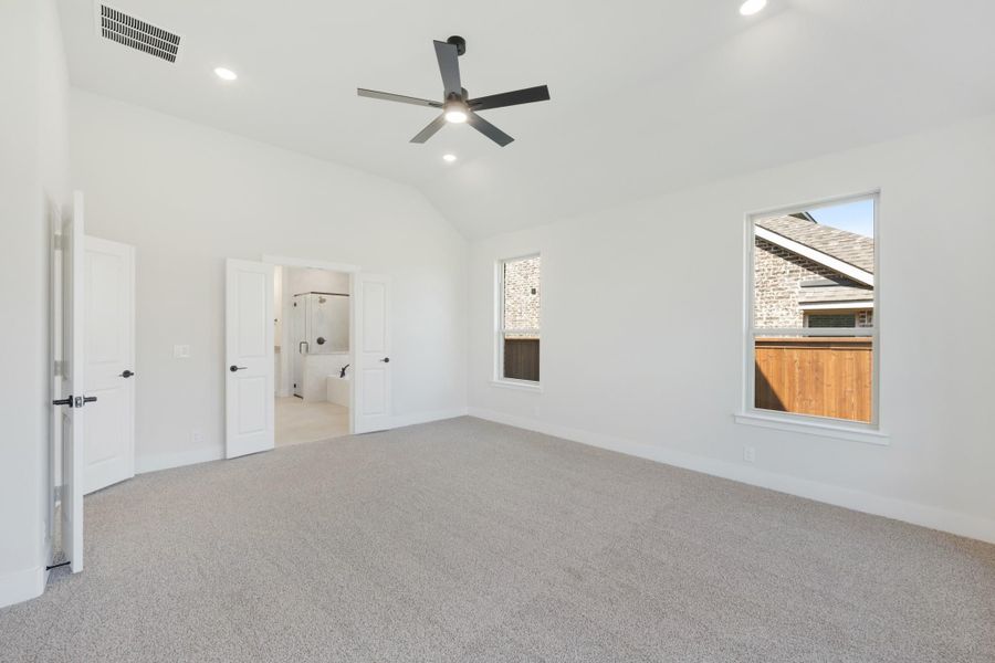 Spacious master bedroom with vaulted ceiling, ceiling fan, carpet flooring, and ensuite bathroom entrance