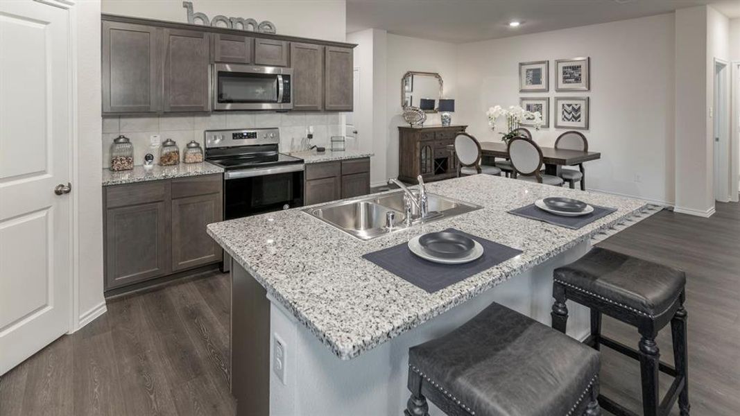 Kitchen featuring dark wood-type flooring, a breakfast bar, stainless steel appliances, dark wood finish cabinets, and light stone counters