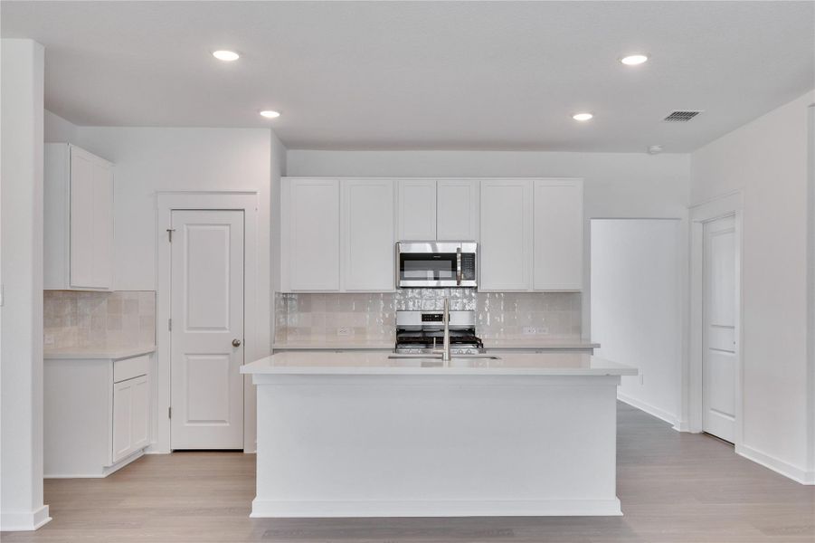 Kitchen featuring white cabinets, stainless steel appliances, decorative backsplash, light wood finished floors, and recessed lighting Kitchen featuring white cabinets, stainless steel appliances, decorative backsplash, light wood finished floors, and recessed lighting