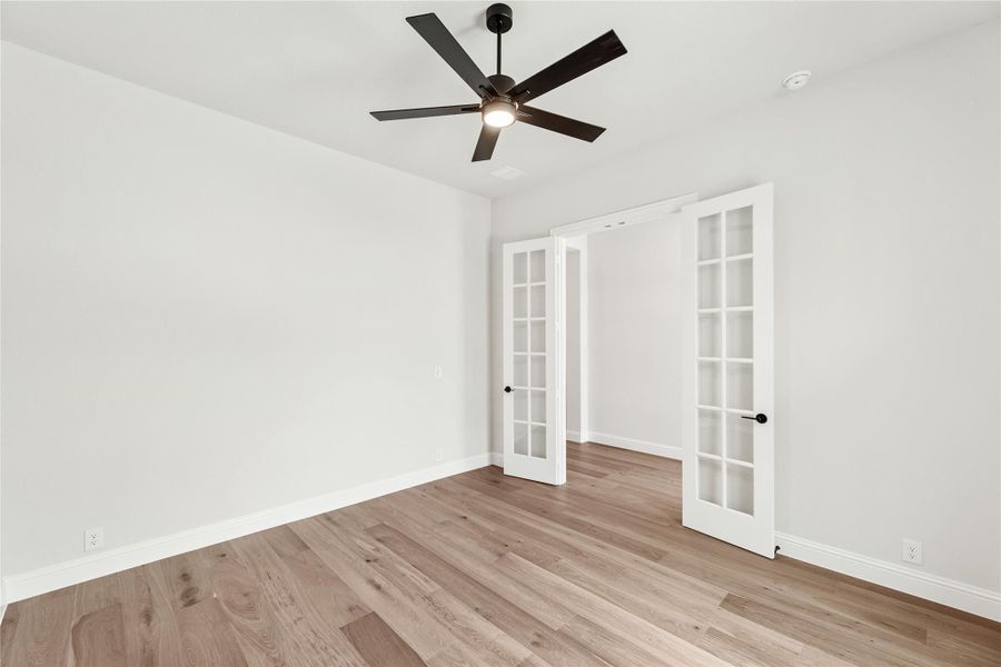 Empty room with light wood floors, white French doors, and a dark ceiling fan