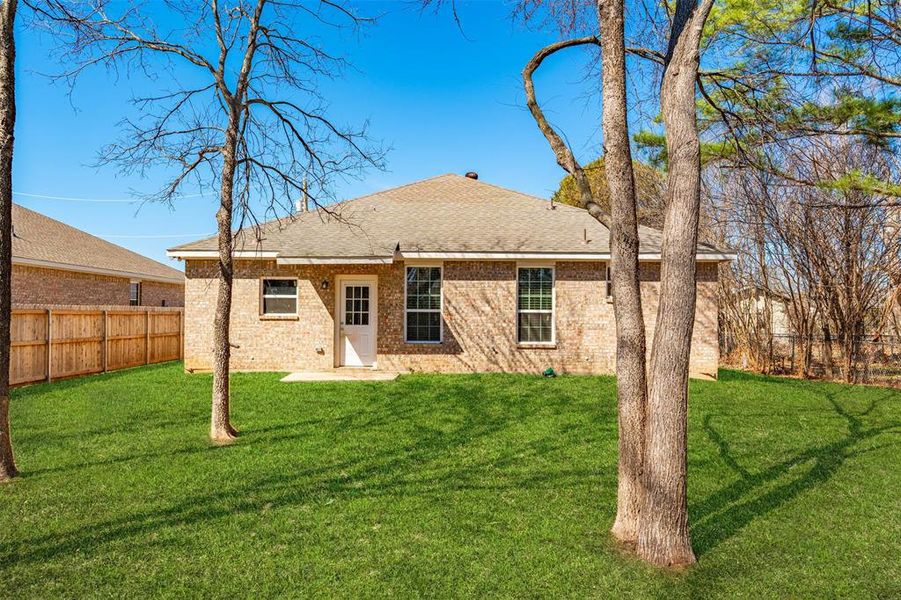 Back of house featuring brick siding, a fenced backyard, a shingled roof, and a yard