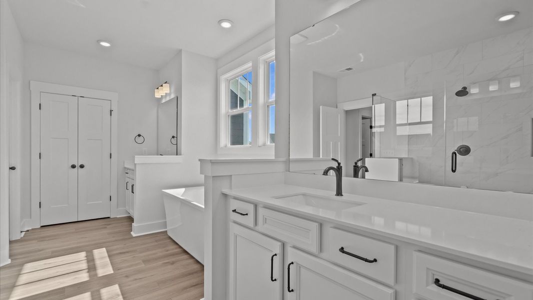 Spacious and modern primary bathroom with tiled walk-in shower, soaking tub, and first-class separate vanity setup
