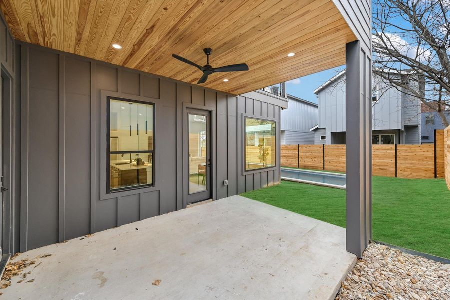 Seamless indoor-outdoor flow. The ground-floor covered patio features the same warm wood ceiling detail, contrasting beautifully against the dark architectural siding. It offers a shaded retreat just steps away from the pool.