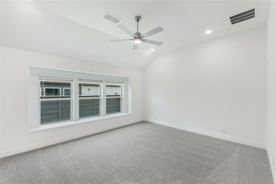 Empty bedroom with vaulted ceiling, ceiling fan, gray carpet, and triple windows with white trim Empty bedroom with vaulted ceiling, ceiling fan, gray carpet, and triple windows with white trim