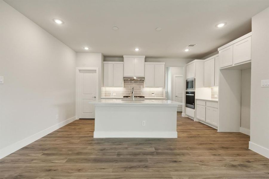 Kitchen with white cabinetry, backsplash, hardwood / wood-style floors, a center island with sink, and appliances with stainless steel finishes