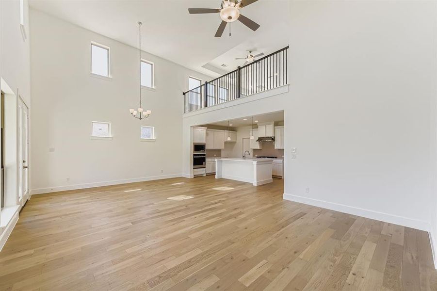 Unfurnished living room with light wood finished floors, a ceiling fan, a high ceiling, and a chandelier Unfurnished living room with light wood finished floors, a ceiling fan, a high ceiling, and a chandelier