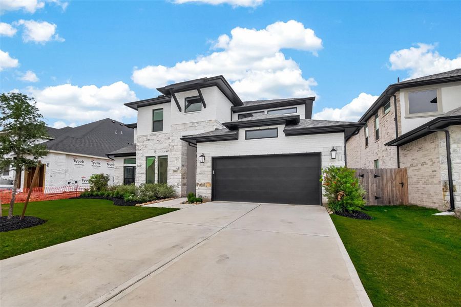 This modern two-story home features a sleek design with a mix of brick and siding, a spacious driveway leading to a two-car garage, and a well-maintained front lawn.