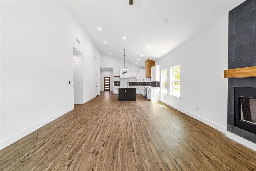 Living room featuring dark wood-style floors, a tile fireplace, recessed lighting, and high vaulted ceiling