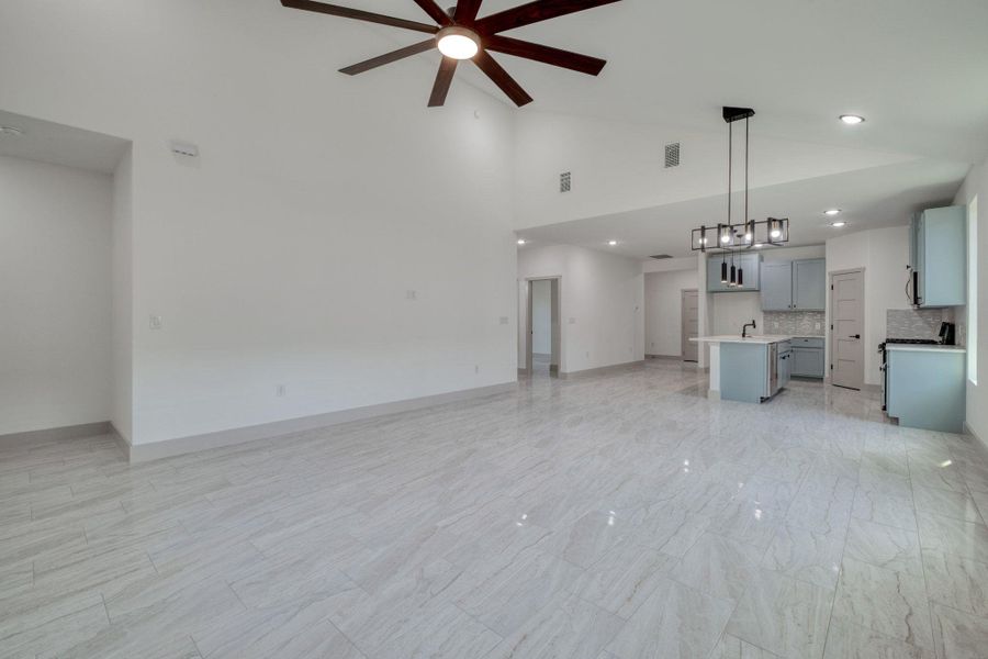 Unfurnished living room featuring ceiling fan and high vaulted ceiling Unfurnished living room featuring ceiling fan and high vaulted ceiling